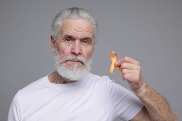 Multiple Sclerosis awareness. Senior man with orange ribbon on grey background