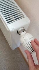 A woman's hand turns the battery heating knob. Heating in an apartment, at home. Heating prices. High quality photo.