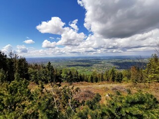 Panoramic view of Beskidy Mountains, Poland, with rolling hills, forests, and villages under a vibrant sky with scattered clouds.