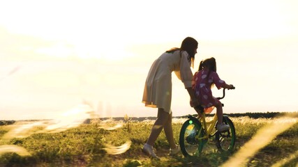 Mother teaching daughter to ride a bike, sunset in the field, family bonding time, childhood memories, summer evening in nature, learning and growing together, mother and child love, outdoor adventure