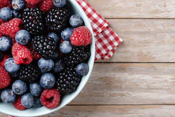 Fresh assortment berries in bowl on wooden table. Top view. Copy space
