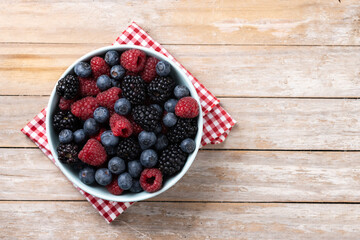 Fresh assortment berries in bowl on wooden table. Top view. Copy space