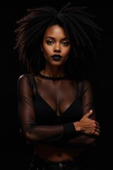 Fototapeta premium Portrait of a young Black woman with dark curly hair and black lipstick, posing in a sheer black top against a black background.