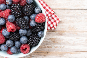 Fresh assortment berries in bowl on wooden table. Top view. Copy space