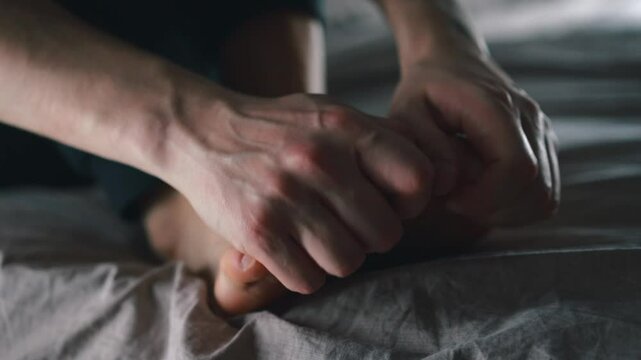 Close-up of toes.
Man stroking his toes with his hand in a dark room.
Man's foot.
Problems with legs.
Pain in legs.
Man massaging toes and feet