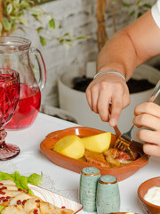 Man cuts meat in wooden plate, potato , compote glass and carafe
