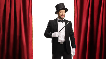 Magician with a magic wand and top hat on a stage with red curtain