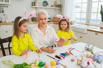 Happy Easter. Two little girls sisters twins grandmother painting eggs enjoying time together....
