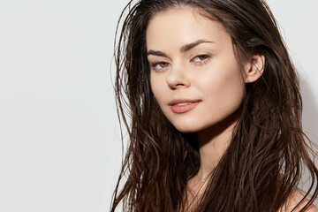 Portrait of a young woman with wet hair, soft makeup, and a serene expression against a light...