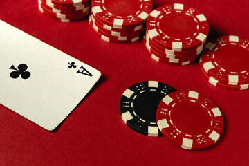 A red table is set for poker with a black and white card showing an Ace of clubs alongside red chips stacked high, evoking excitement in a game night atmosphere