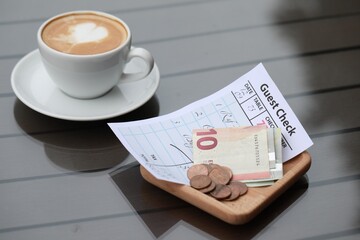 Tip, receipt and cup of coffee on wooden table, closeup