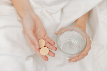 Person in bed holding glass of water and pills
