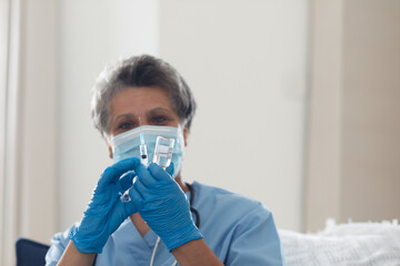 Healthcare professional in blue scrubs preparing syringe with medication at home, copy space