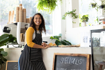 Smiling barista in striped apron serving coffee at cozy cafe counter, copy space