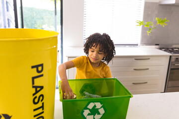 Young boy recycling plastic bottles in kitchen, promoting environmental awareness