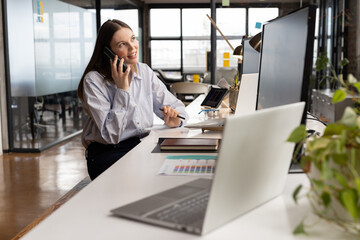 Businesswoman talking on smartphone at office desk, multitasking with laptop, copy space