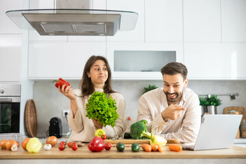 The image captures a joyful moment between a couple cooking with fresh produce and sharing a light-hearted conversation.