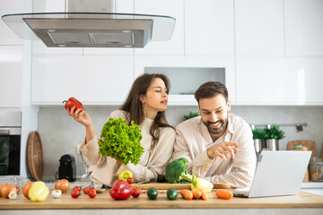 A couple shares a fun cooking experience, laughing and connecting over vibrant fresh ingredients in their modern kitchen.