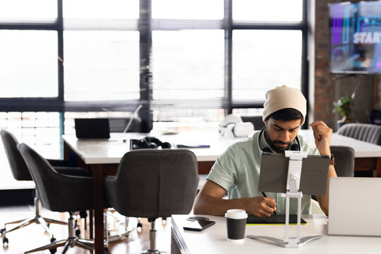 Young man in beanie working on tablet at modern office desk, copy space