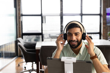 Smiling man in office using headphones and tablet for video conference call, copy space