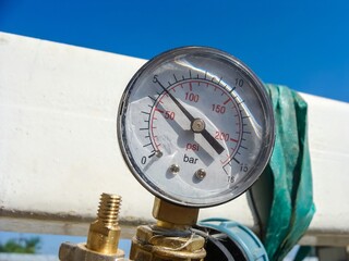 A close-up shows a pressure gauge indicating between 150 and 200 psi, set against a clear blue sky.
