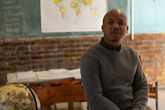African American teacher sitting in classroom with globe and world map, copy space - Powered by Adobe