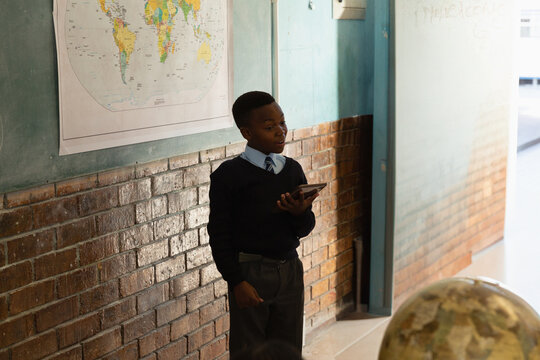 In school, African American boy presenting with tablet in classroom near world map