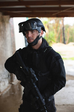 Tactical officer in black uniform holding rifle, standing alert outdoors