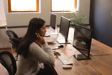 In office, woman multitasking using computer and talking on smartphone efficiently, copy space