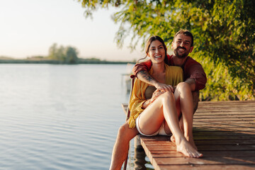 Happy couple smiling and embracing on a wooden pier by the lake at sunset