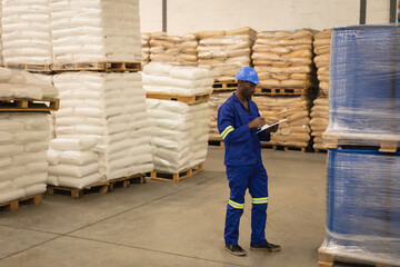 Warehouse worker in blue uniform inspecting inventory and taking notes on clipboard, copy space