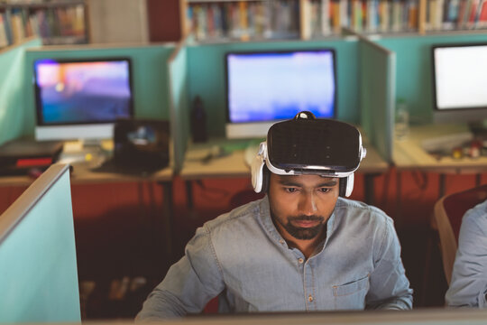 Man using VR headset in office, focused on computer screen, working intently