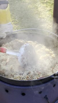 Close up of making traditional plow pilaf rice dish outdoors in a cauldron