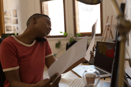 Young professional multitasking with documents and phone call at modern office desk
