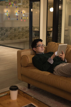 Relaxing at home, Asian man using tablet on sofa, enjoying leisure time, copy space