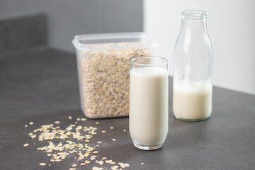 A glass of oat milk and oatmeal in a box on grey kitchen table. Vegan and non-dairy alternative for milk concept