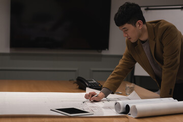 Reviewing architectural blueprints, Asian man focusing on details at conference table, copy space
