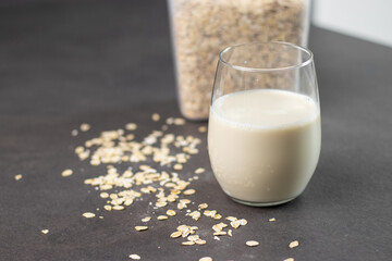A glass of oat milk and oatmeal in a box on grey kitchen table. Vegan and non-dairy alternative milk