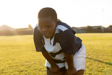 Young female rugby player catching breath on sunny field, showing determination