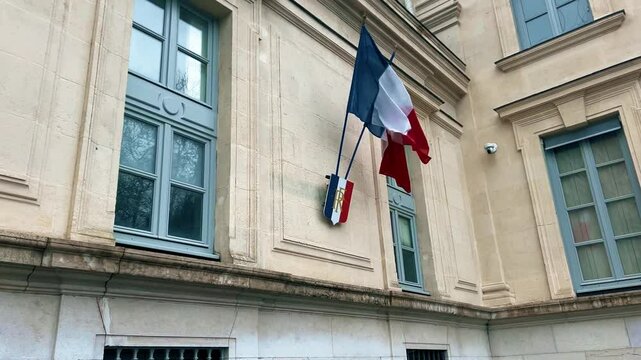 Waving national flags of France and the shield with letters RF Republique Francaise or French Republic on the typical administrative building