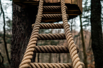 Fototapeta premium A sturdy rope ladder leading up to a wooden treehouse in a dense forest. The close-up view highlights the texture of the thick rope and wooden rungs, creating a rustic and adventurous atmosphere