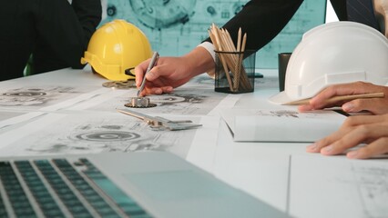 Engineers collaborate on detailed blueprints in a modern office, showcasing design tools,...