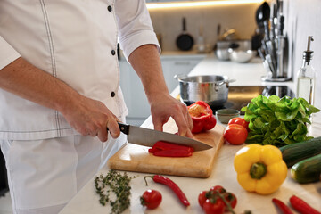 Professional chef cutting bell pepper at counter in kitchen, closeup