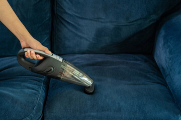 Young maid using handheld cordless vacuum cleaner to vacuuming and cleaning the dust on sofa in home. Housewife using a wireless vacuum machine to cleaner. Housekeeper vacuuming in living room. © Patcharanan