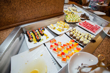 Hotel dessert buffet featuring colorful pastries arranged on white plates. Vibrant sweets create inviting ambiance. Warm lighting complements dessert presentation