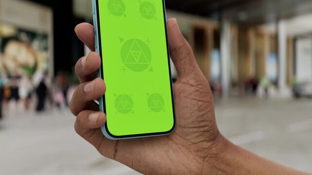 GREEN SCREEN CHROMA KEY Smartphone with a green screen held in a hand near a hotel entrance, featuring a parked car and modern urban surroundings