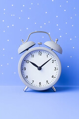 Grey alarm clock on a pastel blue background with small white dots