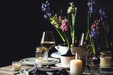 Beautiful elegant table setting for Easter celebration with fresh spring hyacinth flowers, burning candles. Romantic wedding dinner table decoration. Springtime, home gardening. Dark background