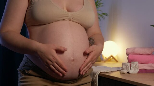 Pregnant woman stroke big belly in anticipation getting ready for the baby boy at home. Future mom at 9 months of pregnancy preparing and planning newborn baby girl clothes
