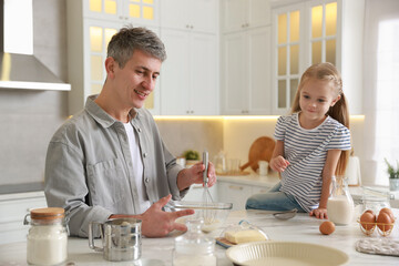 Father and his daughter making dough at white marble table in kitchen